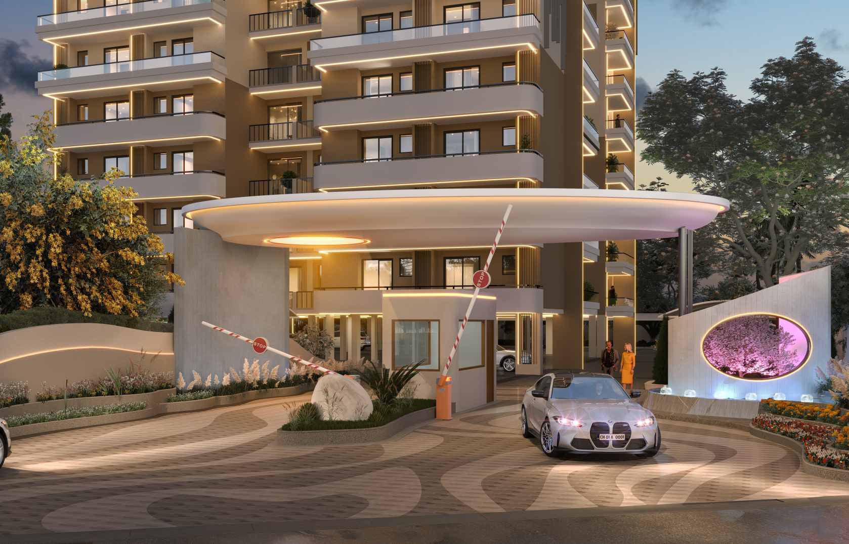 The illuminated entrance driveway of a modern multi-story residential building, showing a security booth, barrier gates, and a car.